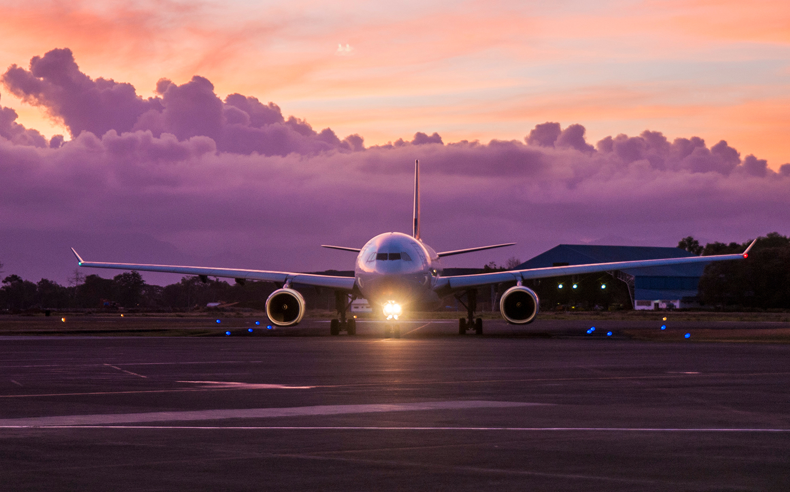 Large airplane with light on runway with pink sunset