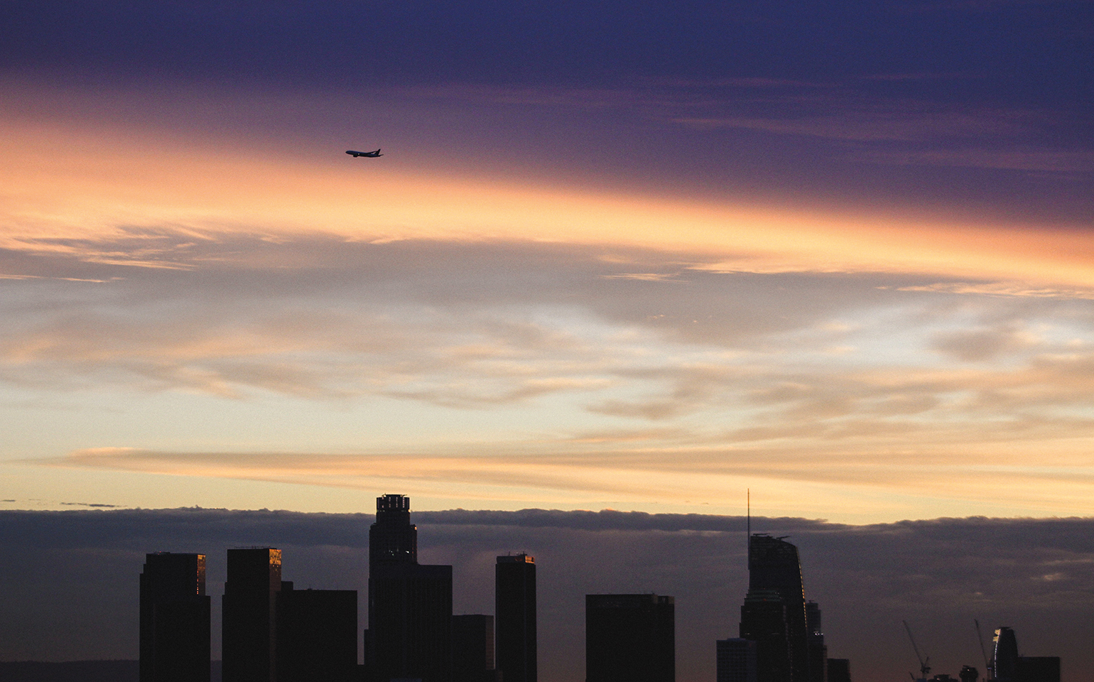 plane far away in a sunset-tined skyline of a major city 